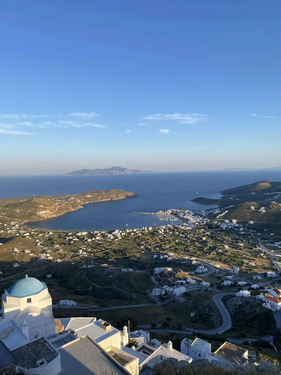 Baie et village blanc des Cyclades vus des hauteurs, dôme bleu d'une chapelle au premier plan, Grèce