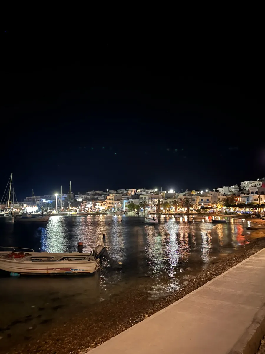 Port grec de nuit, barques amarrées et lumières du village reflétées sur l'eau